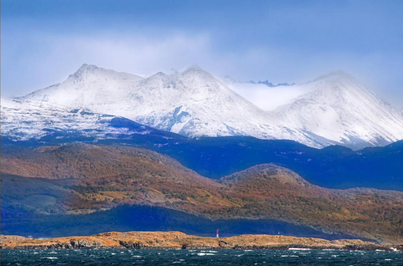 Paisagem da Patagônia fotografada pela Kat: montanhas nevadas, encostas alaranjadas e mar escuro, com o azul e o laranja separados